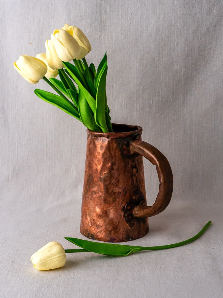 Antique French hand-forged copper tankard with large handle and hammer marks on light surface.