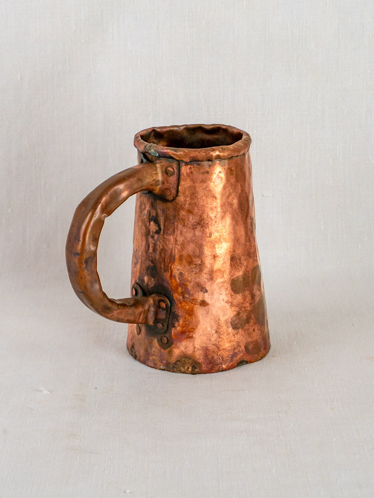 Antique hand-forged French copper tavern tankard with large handle and rustic hammered texture.