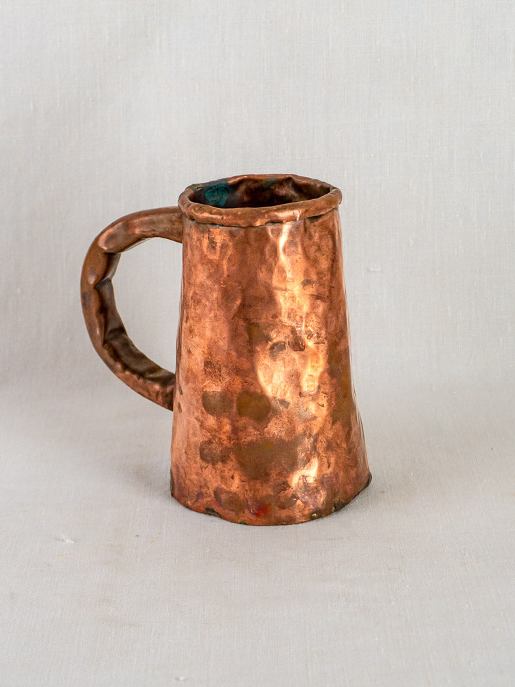 Antique French hand-forged copper chope tankard with hammered texture and sturdy handle on light background.