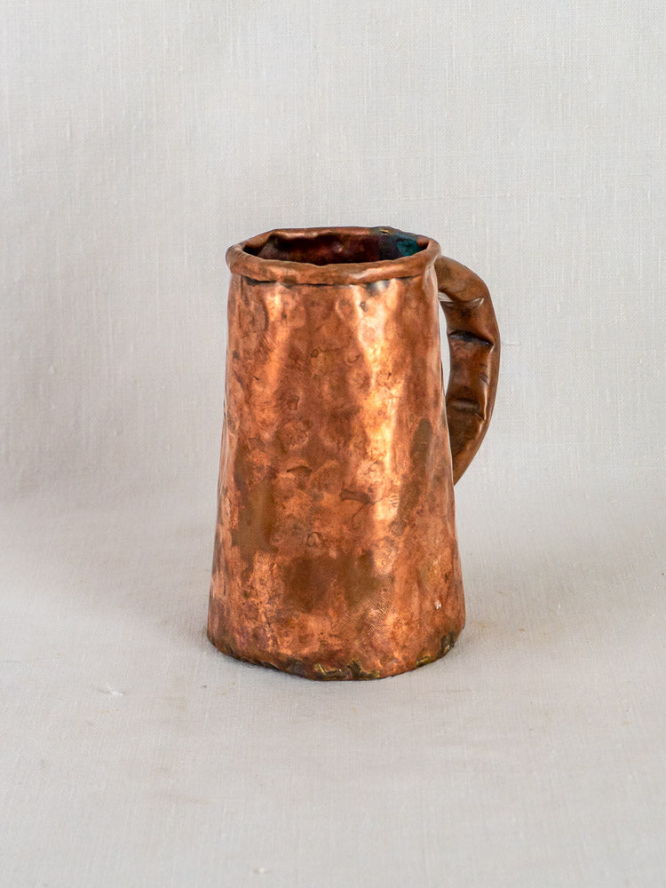 Hand-forged French copper tankard with hammered finish and uneven rim on light gray background.