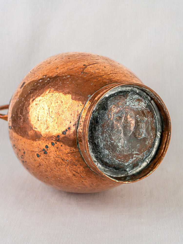 Antique French hand-raised copper double-spout water jug showing textured, timeworn base and patina.