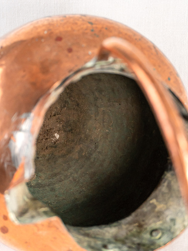 Top view of an antique French copper water jug with double spouts and a jagged, greenish corroded opening.