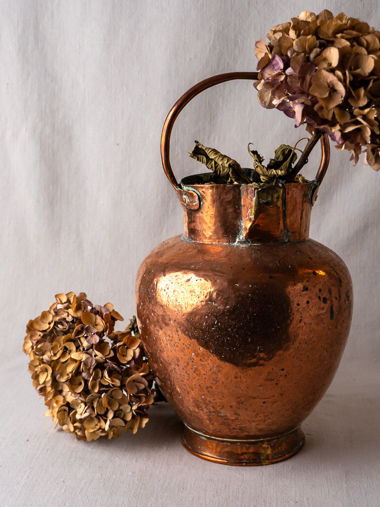 Antique French double-spout copper water jug with hammered finish, filled with dried hydrangeas.