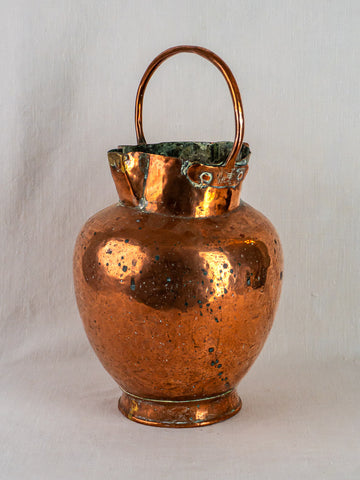 Antique French copper water jug with double spout, scalloped rim, and curved handle on fabric background.