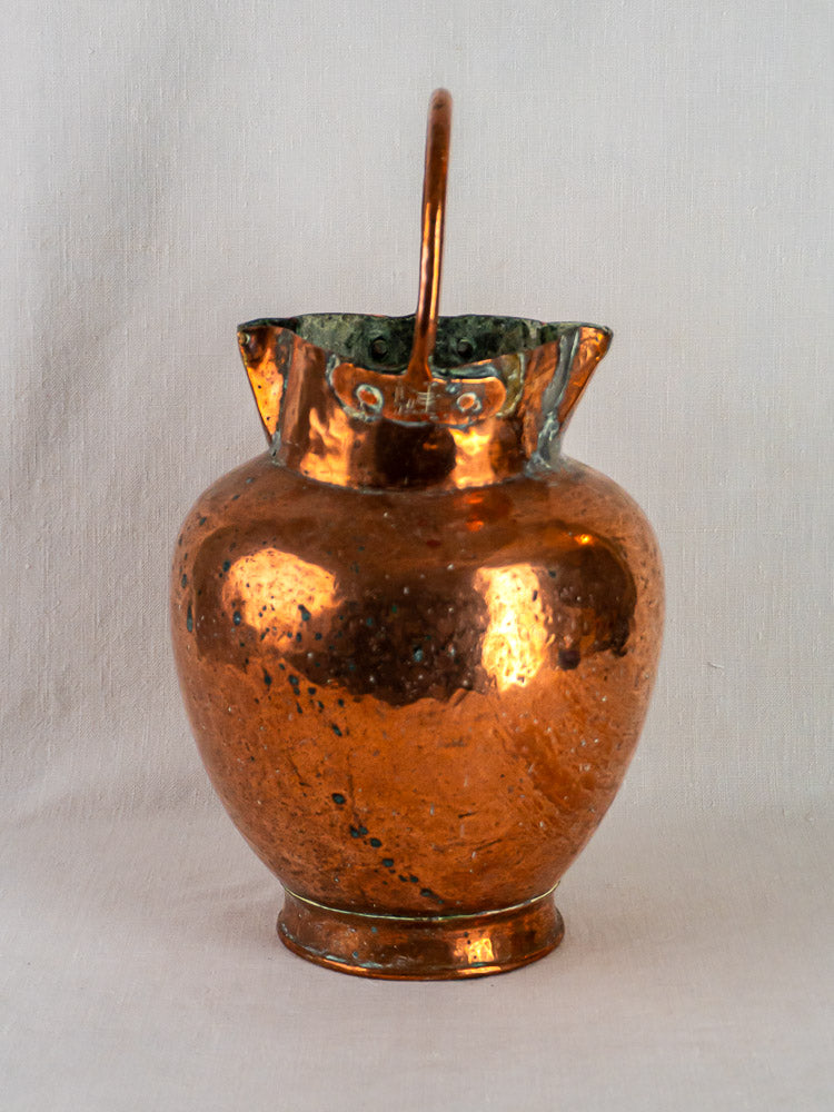 Antique French double-spout copper water jug with curved handle and hammered texture on fabric background.