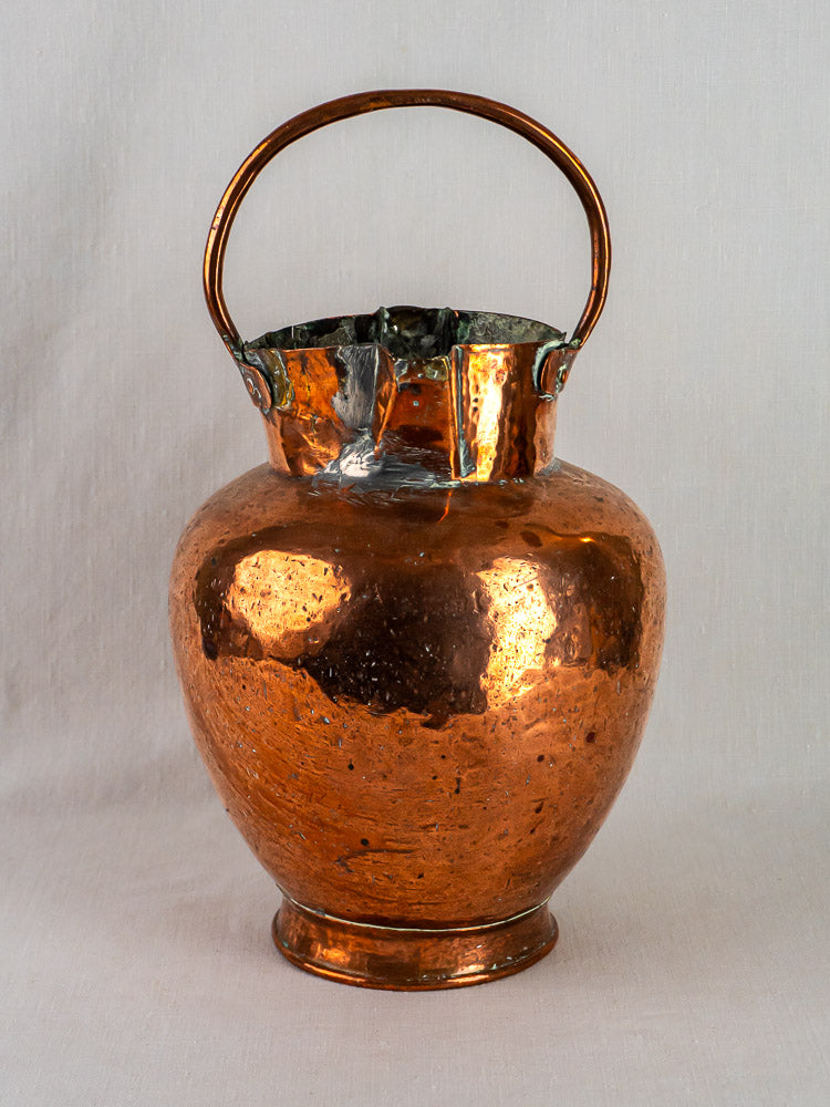 Antique French copper double-spout water jug with hammered finish, arched handle, on light background.