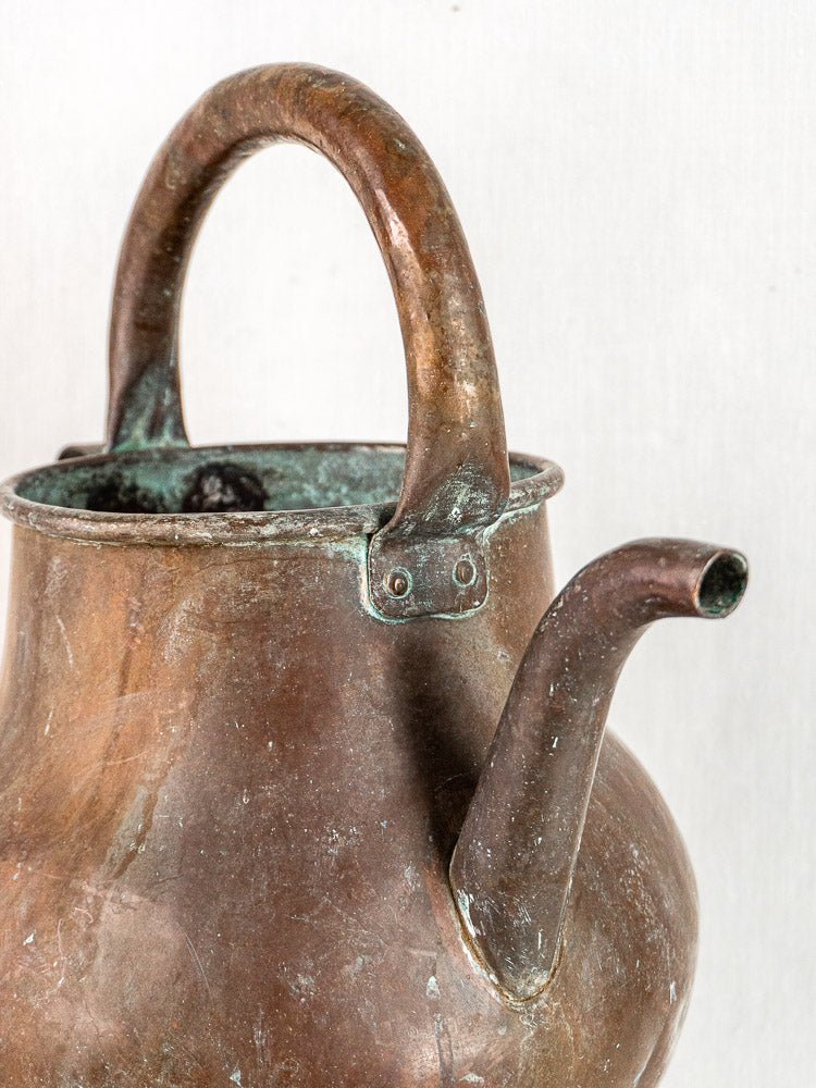 Antique French copper water jug with curved handle and short, angled spout on plain background.