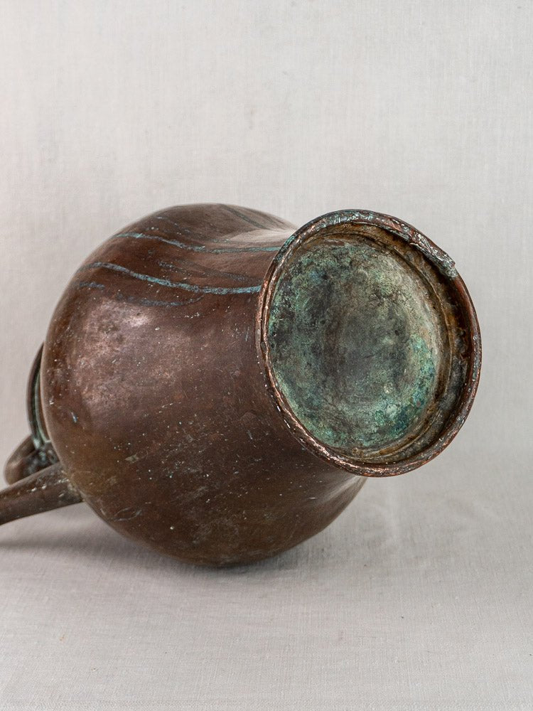 Antique French copper water jug with greenish patina on a neutral textured background.