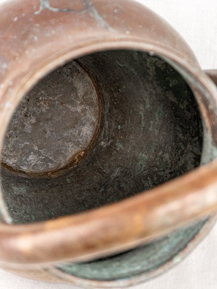 Antique French copper water jug interior with rich patina, verdigris accents, and curved handle detail.