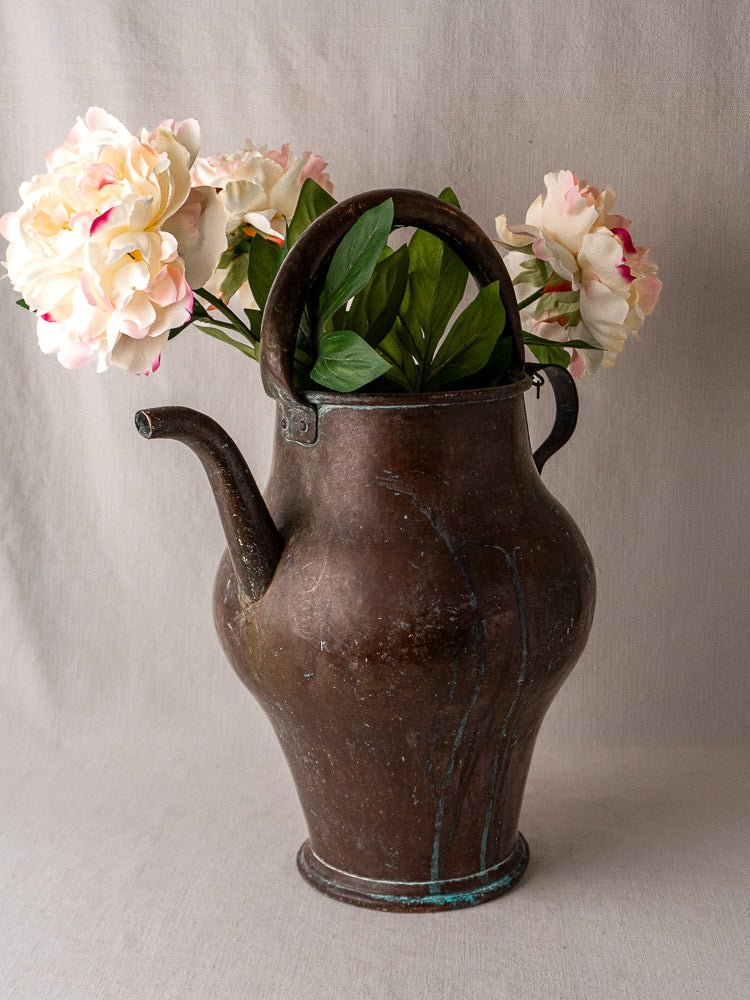 Antique French copper water jug with handle and spout, holding faux pink and white flowers.