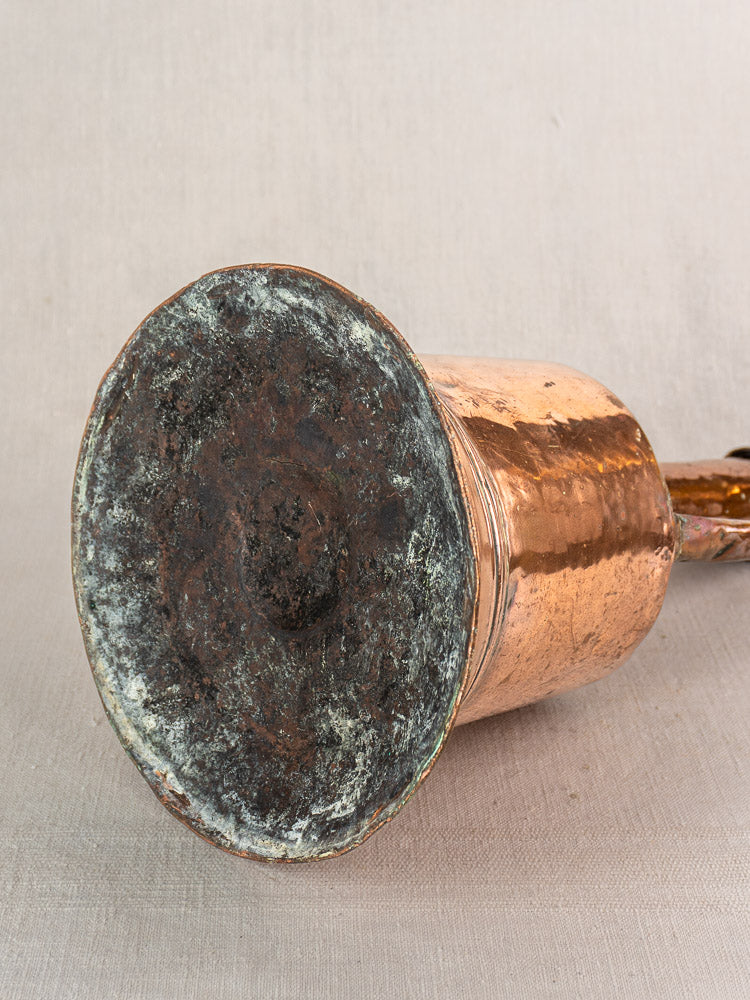 Antique French copper water jug with iron handles, hand-hammered, base tarnished, resting sideways on neutral fabric.