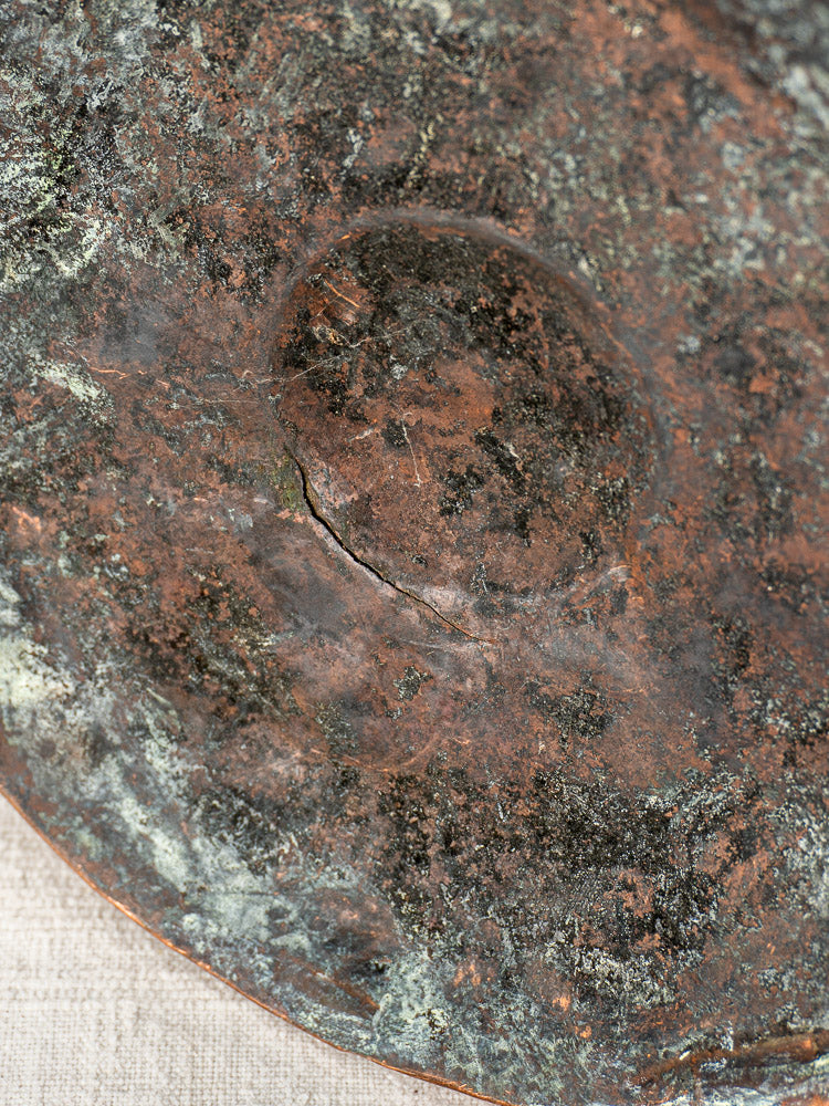 Detail of weathered green and brown patina on domed, cracked French copper water jug with iron handles.