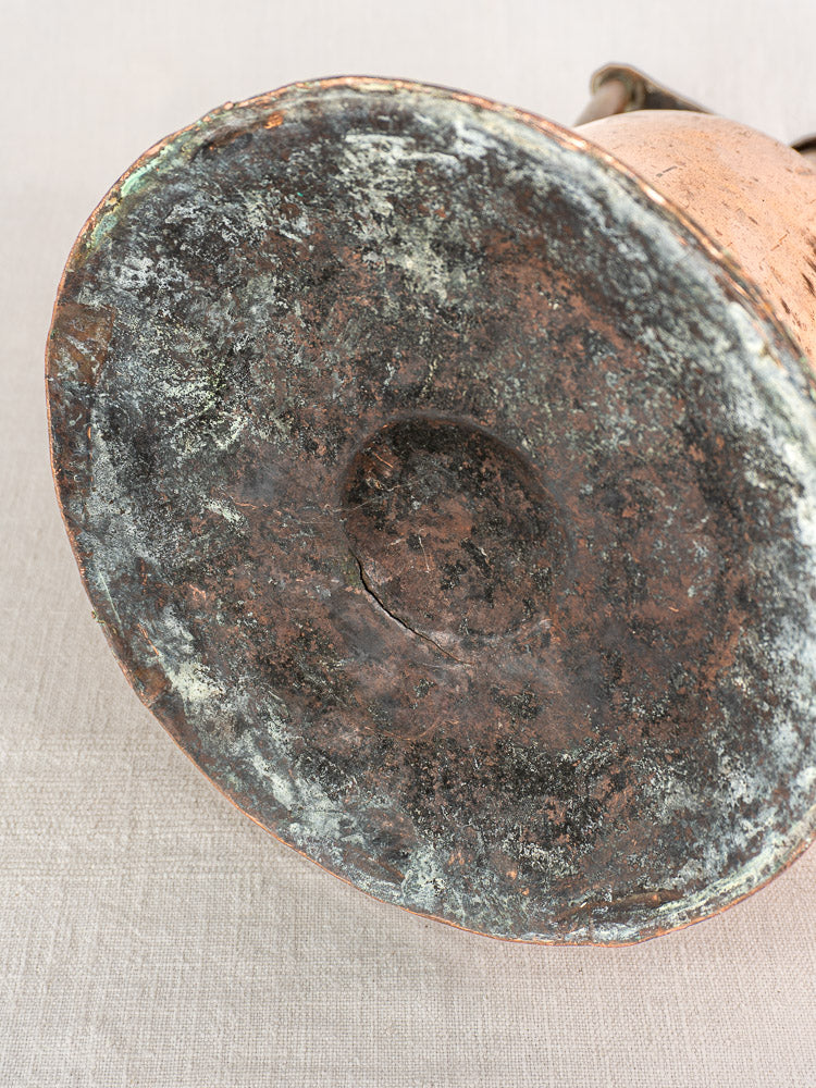 Antique French copper water jug base with iron handles, hand-hammered texture and rich patina on light fabric surface.