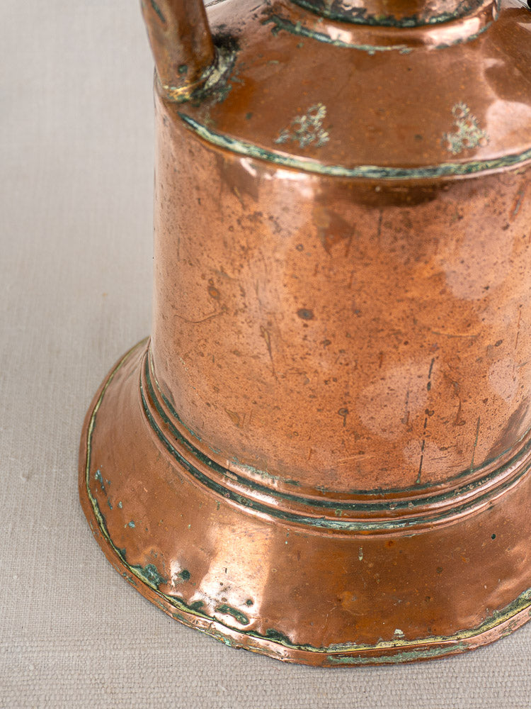 Antique French copper water jug with iron handles, tarnish, green patina, and hand-hammered texture on light fabric.