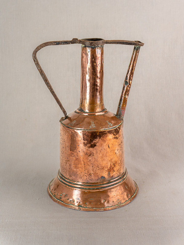 Antique French copper water jug with iron handles, hand-hammered finish, aged patina on neutral fabric background.