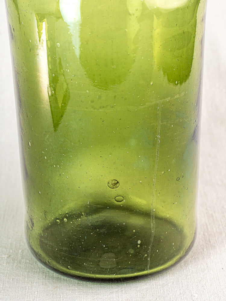 Antique French cornichon jar in hand blown green glass, late 18th century, with visible air bubbles, on textured fabric.