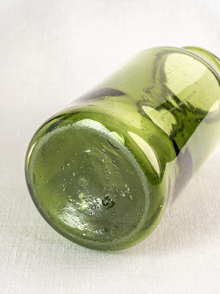 Antique French cornichon jar in hand-blown green glass with visible air bubbles and unique imperfections on a light surface.