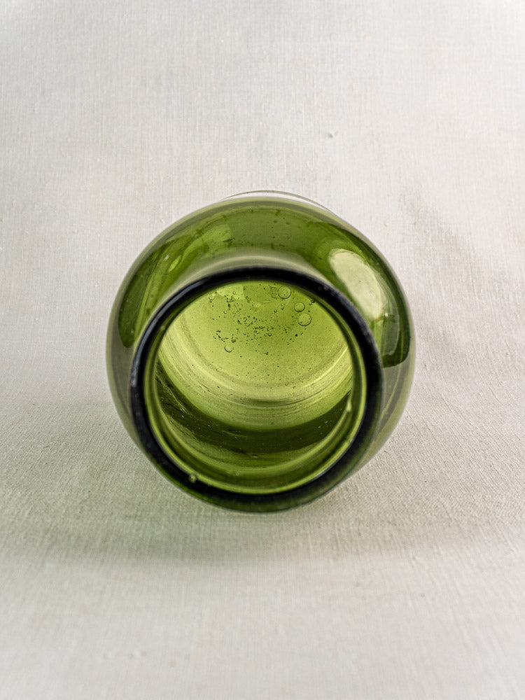 Antique French cornichon jar in hand blown green glass, late 18th century, thick rim, air bubbles, light textured background.