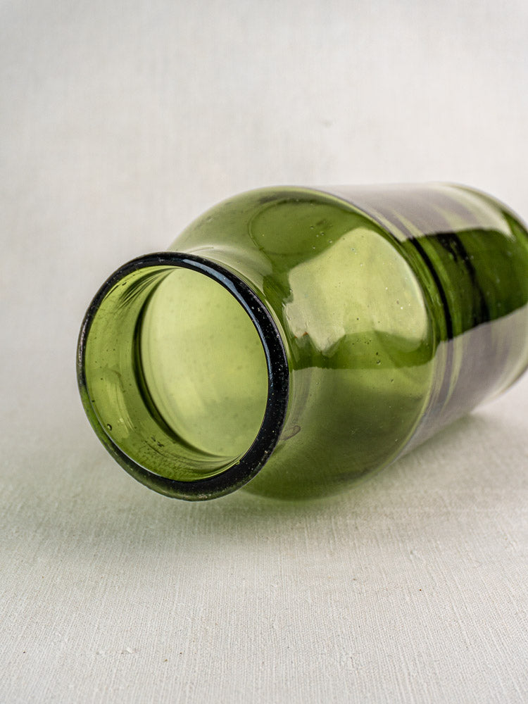 Antique French cornichon jar, hand-blown green glass, late 18th century, on light textured surface, opening facing camera.