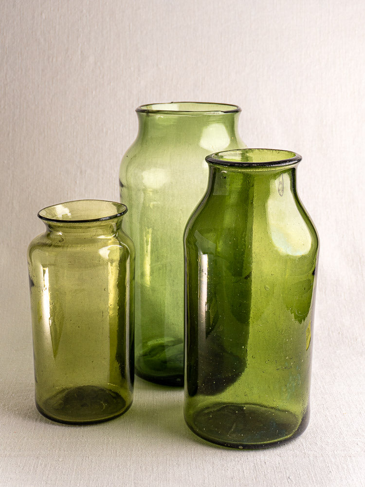 Set of three antique French green glass cornichon jars, late 18th century, grouped on a neutral fabric surface.