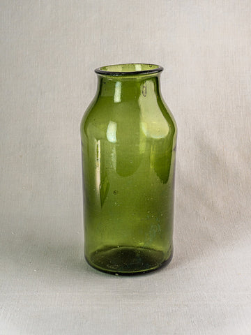 Late 18th-century French hand blown green glass cornichon jar with narrow neck on a light gray textured surface.