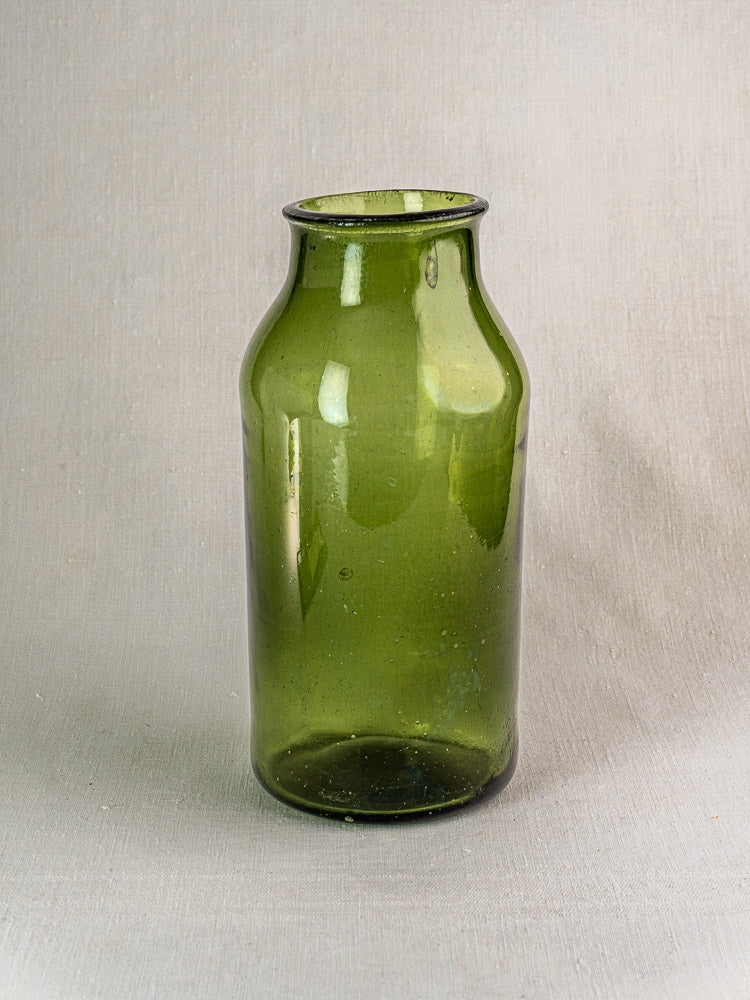 Late 18th-century French hand blown green glass cornichon jar with narrow neck on a light gray textured surface.