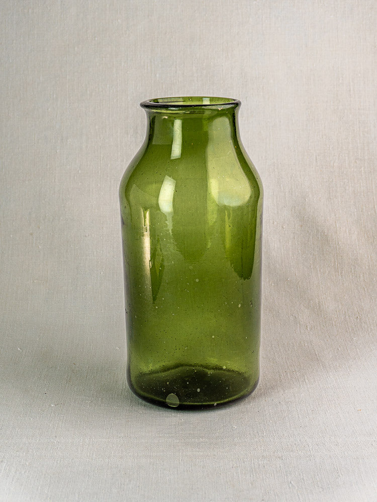Antique French green glass cornichon jar, late 18th century, wide body, short neck on textured light gray surface.