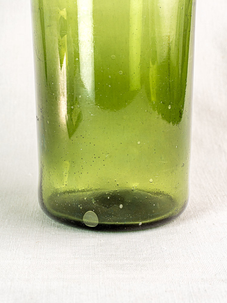 Antique French Cornichon jar, late 18th century hand-blown green glass with air bubbles, on textured light surface.