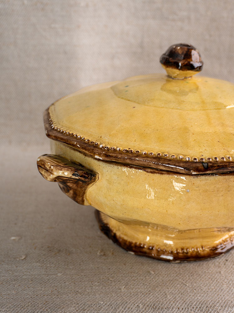 Antique French Vallauris Beretta et Cie pottery casserole with mustard glaze and brown accents on beige fabric.