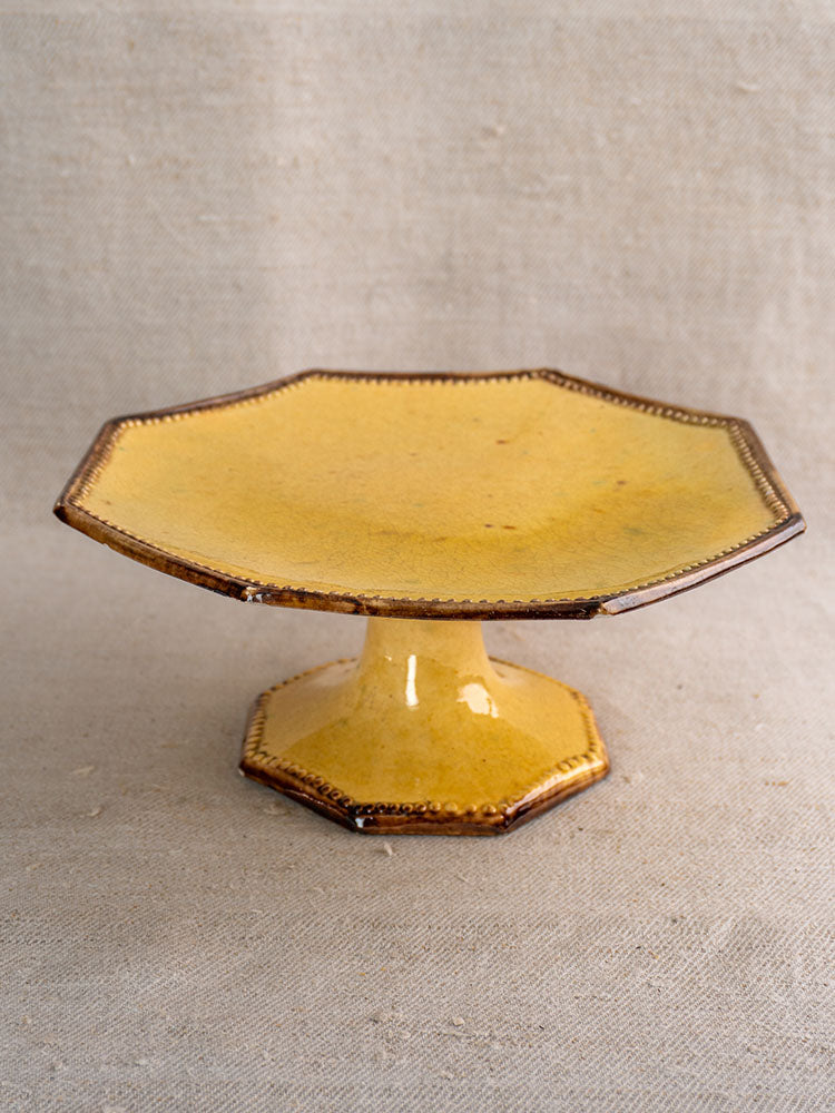 Mustard-glazed octagonal ceramic cake stand by Vallauris Beretta et Cie on beige textured fabric, from a three-piece set.