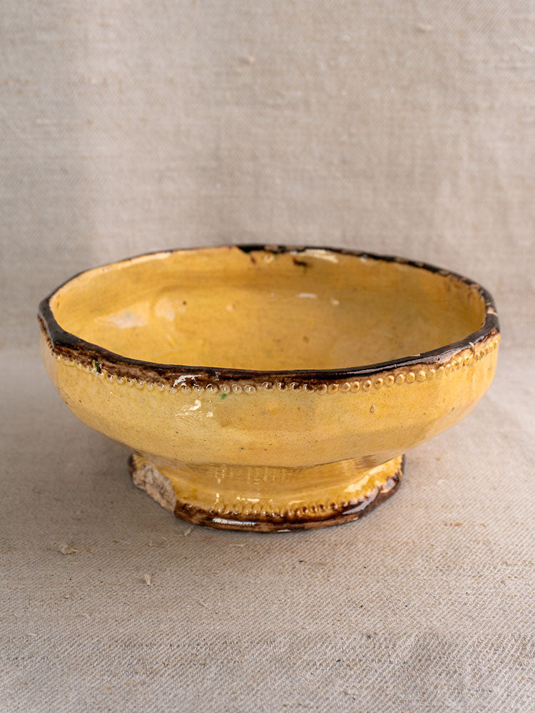 Antique French Vallauris Beretta et Cie pottery set with mustard glaze, dark rim, and textured dots on beige fabric.