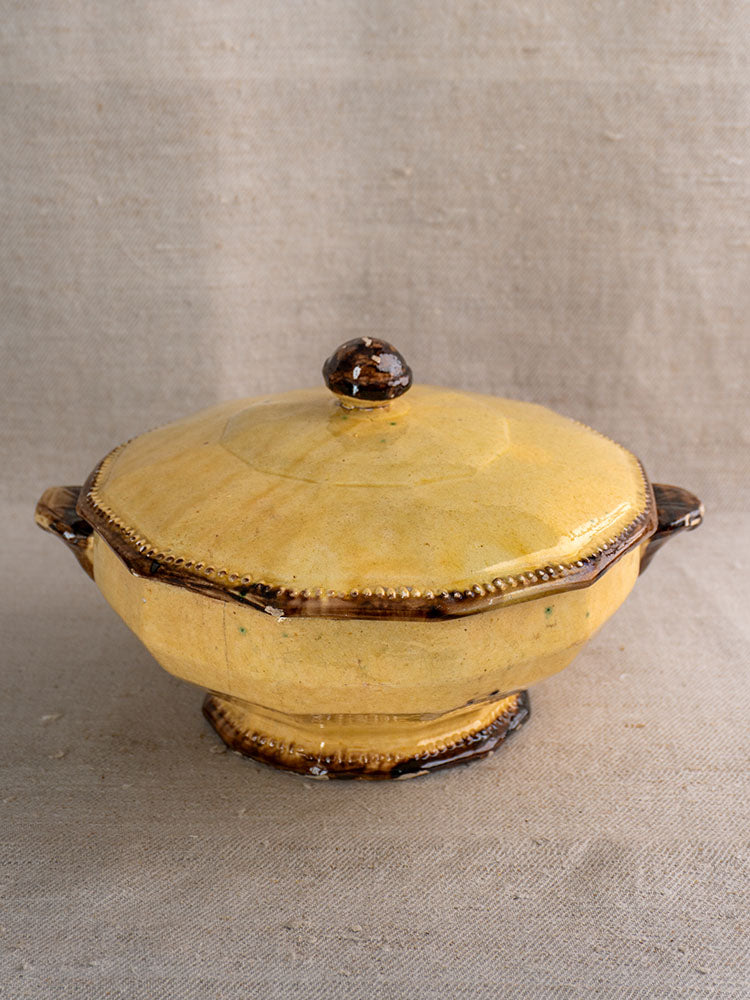 Mustard-glazed Vallauris ceramic soup tureen with lid and handles, brown edging, on neutral fabric.