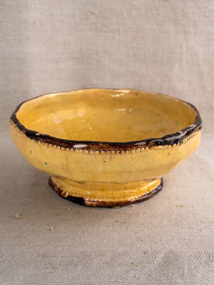 Handcrafted Vallauris Beretta et Cie ceramic bowl with mustard glaze, dark brown rim and base, on textured beige fabric.