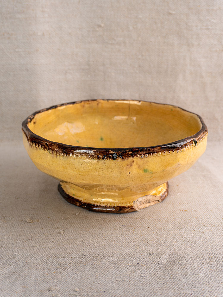 Handmade Vallauris Beretta et Cie bowl with mustard glaze, dark brown rim, beaded edge; on textured beige fabric.