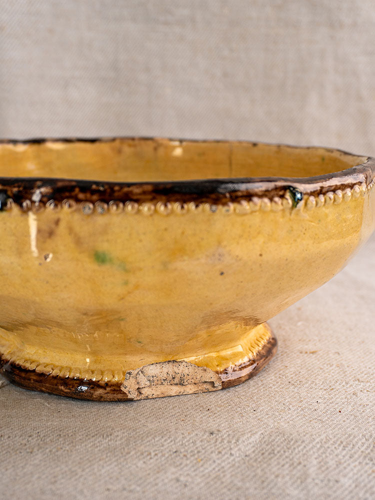 Shallow yellow ceramic bowl with brown rim and beaded edge by Vallauris Beretta et Cie on beige fabric.