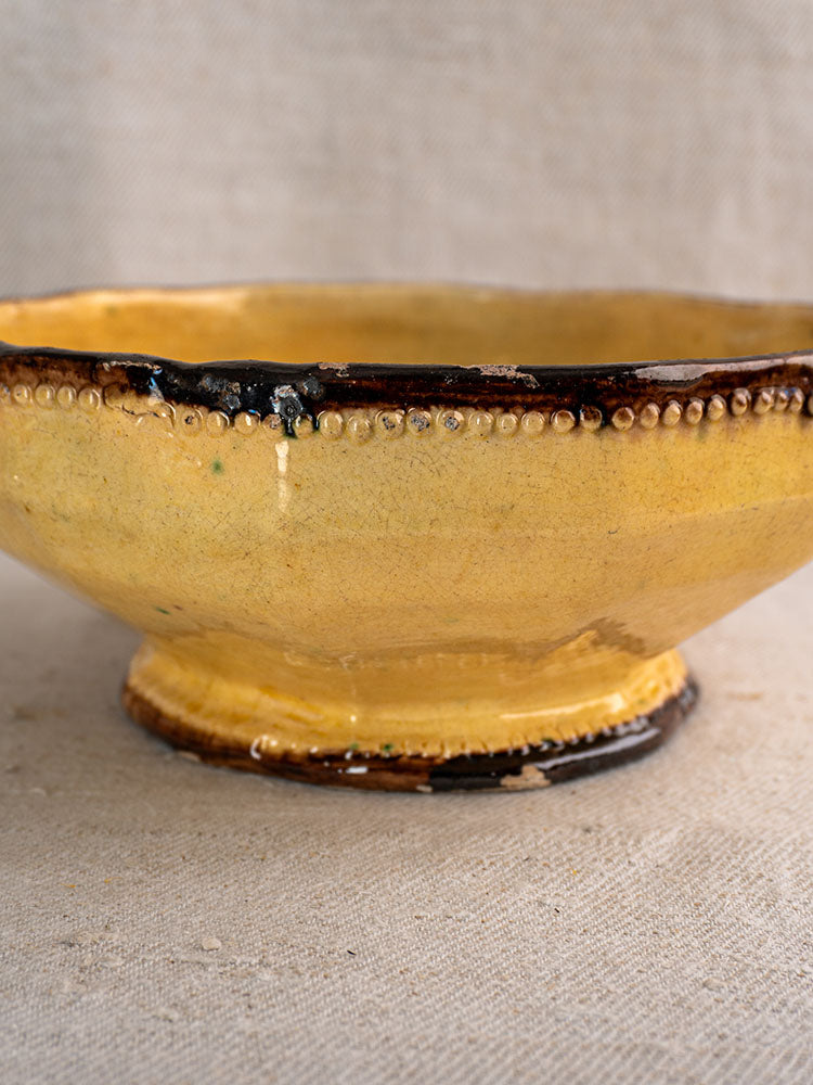 Mustard yellow Vallauris ceramic bowl with dark brown rim and base, dotted band, on neutral fabric.