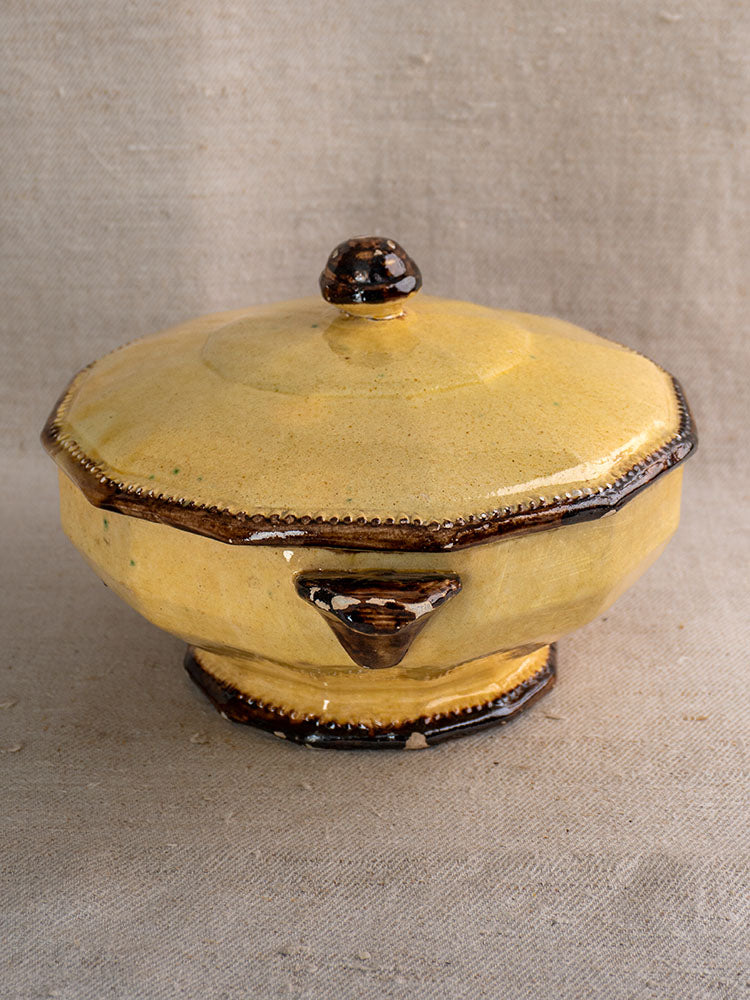 Yellow ceramic lidded bowl with brown accents by Vallauris Beretta et Cie on textured beige fabric.