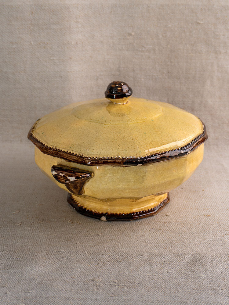 Mustard-glazed octagonal Vallauris Beretta et Cie tureen with dark trim on neutral fabric background.