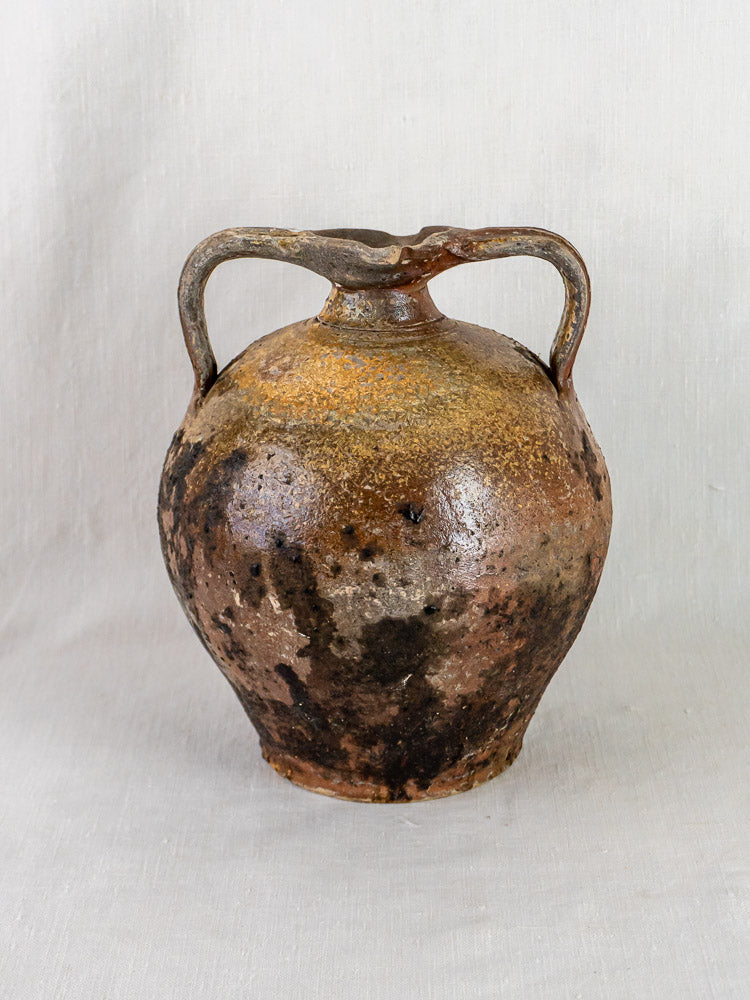 Antique French Orjol terracotta pouring jar with two handles and rich brown-black tones on light fabric.