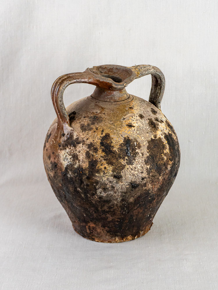 Antique French terracotta orjol with two handles, weathered surface, and dark patches on plain background.
