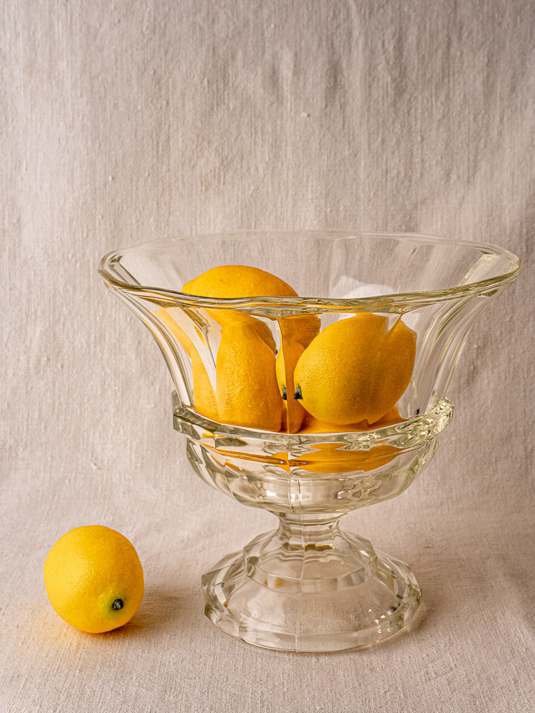 Antique French glass coupe Médicis compotier with yellow lemons on a light fabric surface.