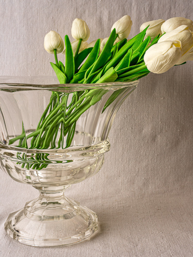 Antique French glass Coupe Médicis compotier with white tulips on beige fabric backdrop.