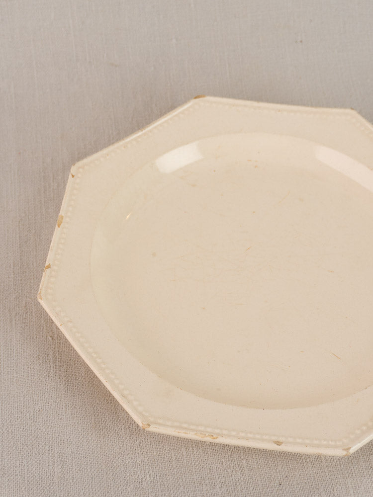 19th-century French creamware plate with octagonal beaded rim displayed on a textured grey surface.