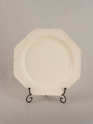19th-century French creamware octagonal plate with beaded rim on black metal stand, neutral gray backdrop.