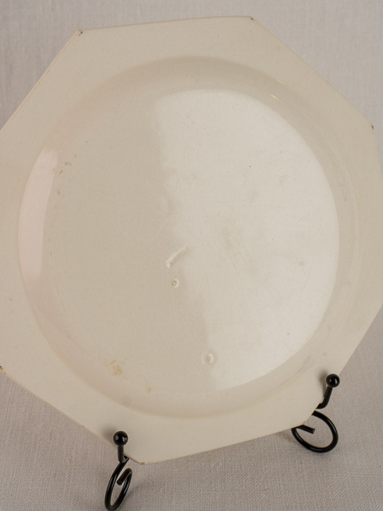 Antique French creamware plate with octagonal beaded rim on black metal stand, light background, minor marks visible.