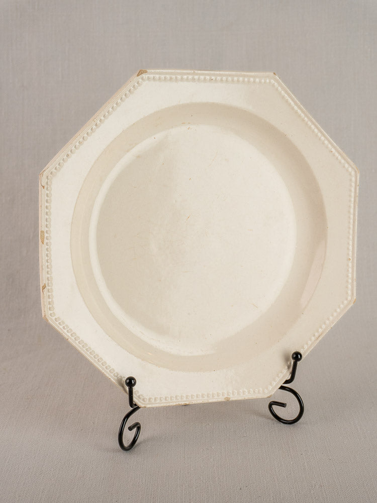 19th-century French creamware plate with octagonal shape and beaded rim on black stand, neutral gray background.