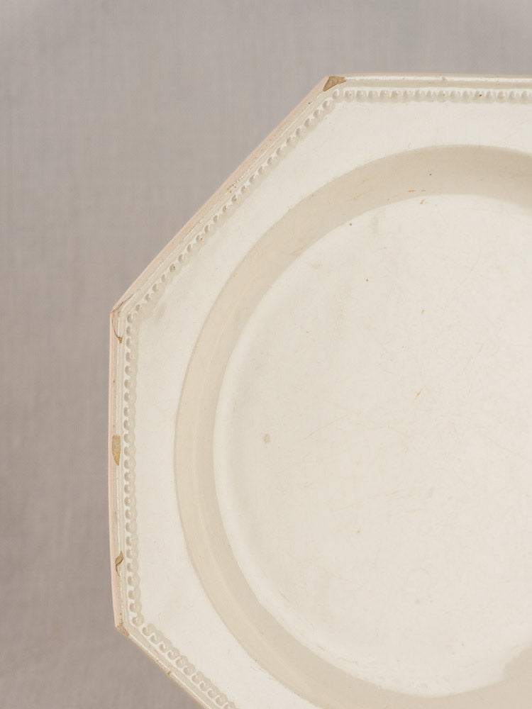 Antique French creamware plate, 19th century, octagonal beaded rim with edge wear and chips on plain light background.