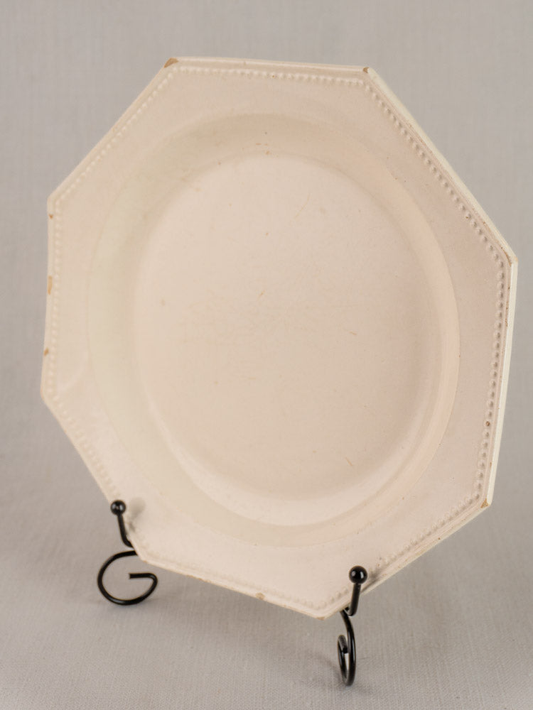 Antique French creamware plate, 19th century, octagonal with beaded rim on black stand, light gray background.