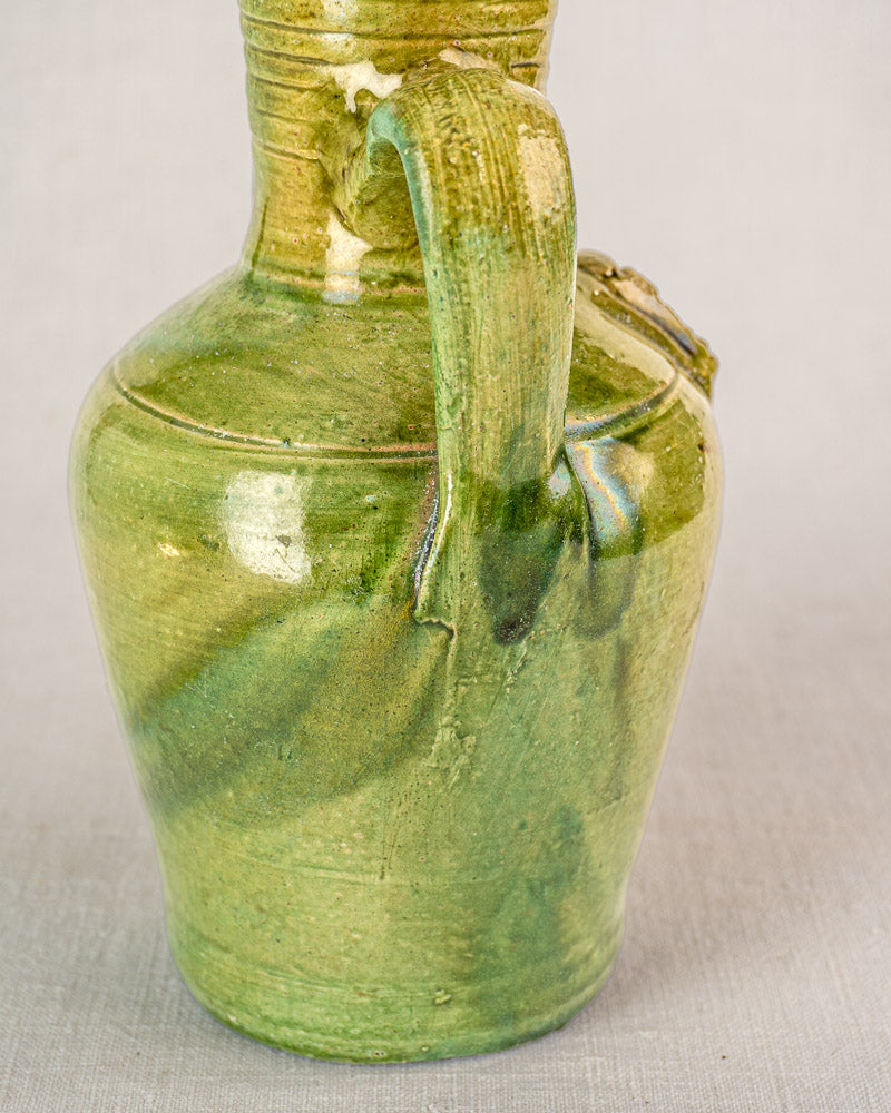 Antique French green glazed earthenware cruche with single handle, curved spout, and medallion on light background.