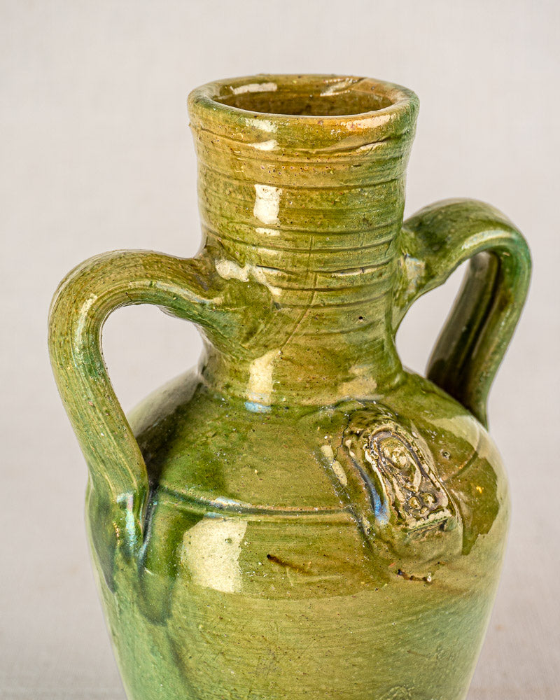 Antique French green glazed earthenware cruche with devotional medallion, two handles, and narrow neck on plain background.
